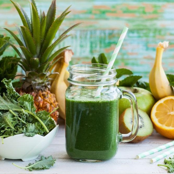 A mason jar filled with green juice and a straw, surrounded by fresh ingredients including pineapple, kale, kiwi, lemon, and banana, highlighting a healthy juice recipe from a wellness ebook.