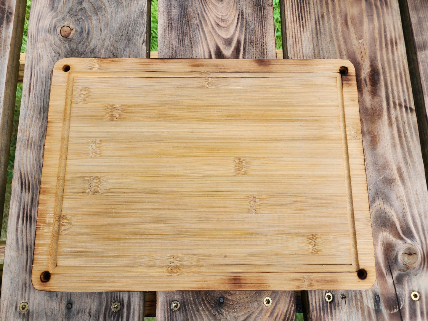 Custom Engraved Cutting Board's A 9.5 x 13 bamboo cutting board displayed flat on a rustic wooden table. The cutting board has rounded corners and small holes in each corner, showcasing its functional yet stylish design. The natural bamboo grain and smooth surface make it a durable and eco-friendly addition to any kitchen for chopping or serving. Custom Engraved Cutting Board's